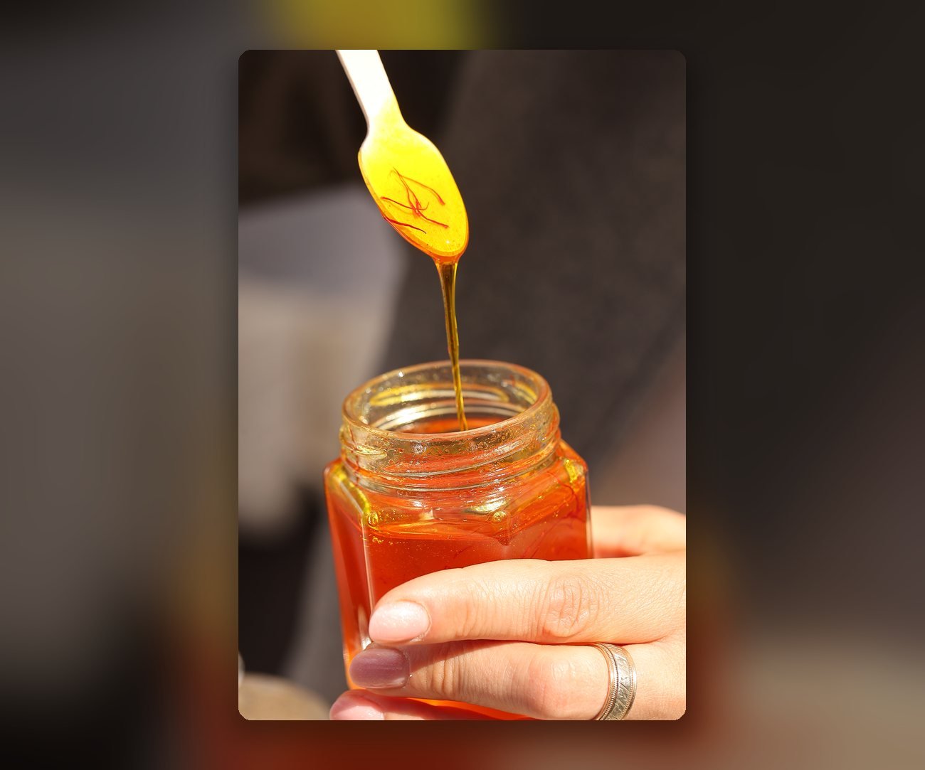 Miere aurie cu fire de șofran turnată din lingură într-un borcan